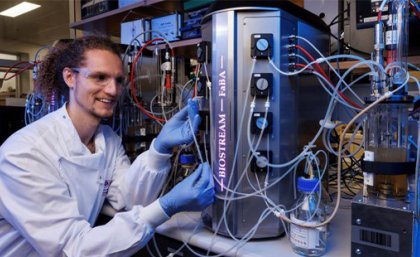 Dr James Heffernan working with a FaBA-funded bioreactor at the UQ Australian Institute for Bioengineering and Nanotechnology. A man in a white coat and blue gloves sits in front of a silver cannister